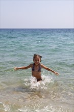 Young smilling girl playing at the sea throwing water and laughing. Photo : Athanasios Papadopoulos