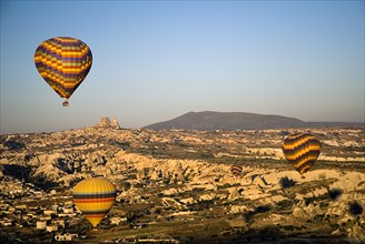 Hot air balloons in flight over landscape in early morning sunlight with Uchisar town in background