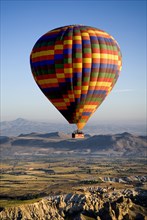 Brightly coloured hot air balloon in flight over the landscape in early morning sunshine. Photo: