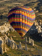 Brightly coloured hot air balloon in flight over rock peaks and pinnacles of Love Valley in early