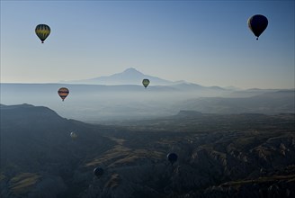 Early morning with hot air balloons in flight mist drifting across landscape and Mount Erciyes in