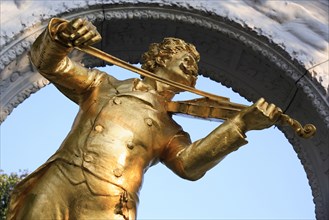 Angled part view of statue of Johann Strauss in the Stadt Park framed by stone arch. Photo :