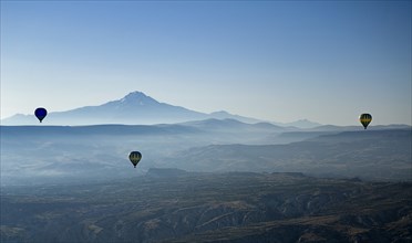Early morning with hot air balloons in flight mist drifting across landscape and Mount Erciyes in