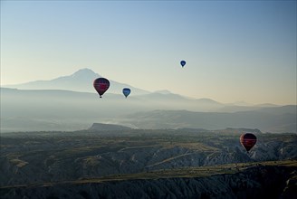 Early morning with hot air balloons in flight above tufa landscape with Mount Erciyes in the