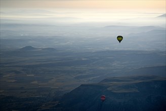 Hot air balloons in flight over landscape in misty early morning light with pale orange sky. Photo: