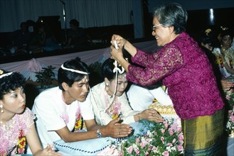 Couple being symbolically bound together with cotton at Thai Buddhist wedding ceremony. Photo :