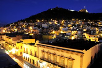 Mexico, Bajio, Zacatecas, View across city rootftops illuminated at night towards Cerro de la Buffa