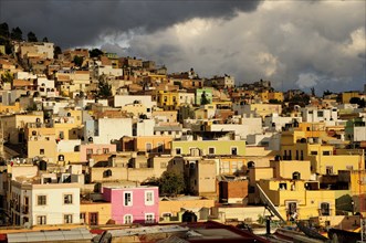 Mexico, Bajio, Zacatecas, Colourful houses clinging to the hillside below sky of thick grey cloud.