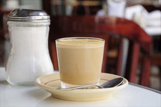 Mexico, Veracruz, Cafe con leche. Coffee with milk served in glass with saucer and spoon on table