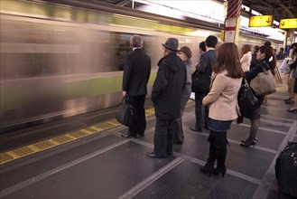 Japan, Honshu, Tokyo, Commuters waiting on platform whilst train speeds through without stopping.