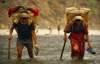 Nepal, East, Arun River Valley, Porters carrying laden baskets fording the Piluwa Khola river.