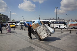 Turkey, Istanbul, Eminonu man transporting rubbish by handcart across the square outside the new