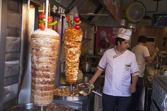 Turkey, Istanbul, Sultanahmet man in kebab restaurant carving shawarma from skewered meats. 
Photo