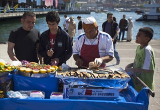 Turkey, Istanbul, Karakoy Galata fish market man selling freshly grilled fish served in bread roll.
