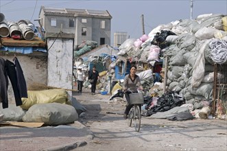 China, Jiangsu, Qidong, Female workers one on a bicycle leaving a recycling depot bundles of waste