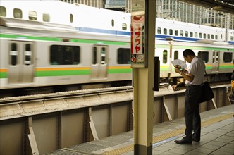 Japan, Honshu, Tokyo, Commuter on platform cooling himself with paper fan whilst waiting for his