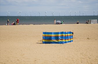 Wind Farm offshore on the horizon with families and windbreaks on the beach.