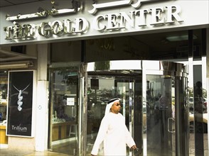 Emirati Arab man in Dishdasha passes Gold Center at Gold Souk Deira.