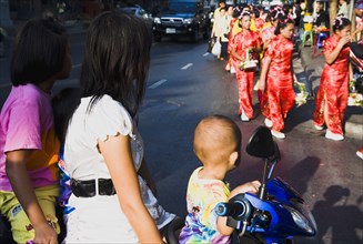 Mother with three children on motorcycle watching parade celebrating local temple.