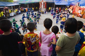 Thai children watch dance troupe at local temple from elevated stage.