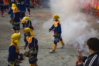Thai boys in Chinese character costume in dance troupe with firecrackers exploding at local temple.
