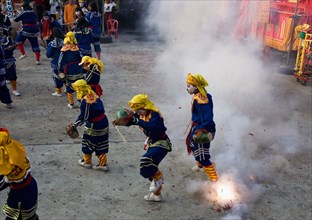 Thai boys in Chinese character costume dancing and drumming with firecrackers exploding at local temple.