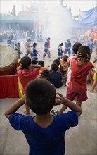 Thai boys cover their ears watching performance with firecrackers exploding at local temple.