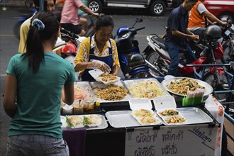 Street vendor and daughter sell take away Pad-thai the national fried noodle classic dish.