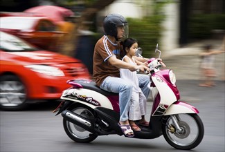 Father with young daughter on motorcycle pass brightly coloured taxis.