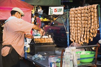 Street vendor selling sausages in early evening light 5 Baht each cheapest food in the city.