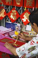 Calligrapher painting Gold characters on red paper auspicious colours for Chinese New Year.