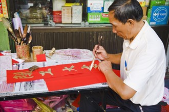 Calligrapher painting Gold characters on red paper auspicious colours for Chinese New Year.