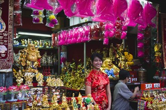 Young woman in Cheong sam chinese dress at shop selling decorations for Chinese New Year.
