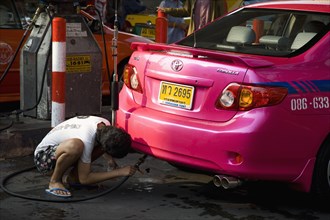 Pink metered taxi cab being refuelled with LPG gas pipe.