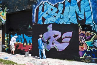 Graffiti artists painting wall.