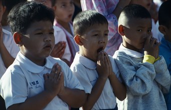 Buddhist Schoolchildren with hands held in prayer one child yawning.