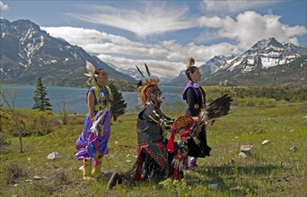 Blackfoot Indians dressed for a Pow Wow with Middle and Upper Waterton Lakes the Rocky Mountains and the Prince of Wales Hotel in the background. The park is a UNESCO World Heritage Site Blue sky with...