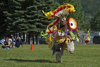 Blackfoot dancer in the Men's Fancy Dance at the Blackfoot Arts & Heritage Festival Pow Wow organized by Parks Canada and the Blackfoot Canadian Cultural Society Tourists sitting on grass watching spe...