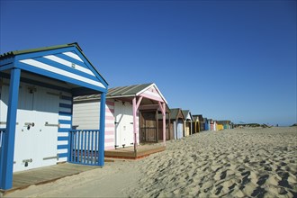 Colourful beach huts along sandy beach.
