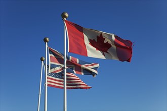 Canadian, British and United States of America flags flying against a blue sky.