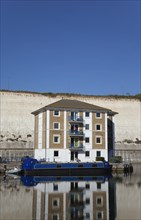 Apartment building in marina with moored barge and chalk cliffs behind.