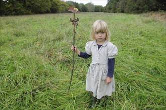 5 year old Eva with stick & leaf flag in a field of grass.