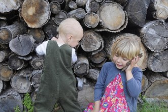 5 year old Eva and Oscar aged two playing beside a log pile with Eva using bark as pretend mobile phone.