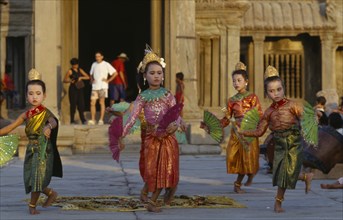 Cambodia, Angkor, Angkor Wat, Child dancers in traditional dress with tourists framed by temple