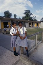 West Indies, Jamaica, Education, Two schoolgirls in checked dresses in playground in front of