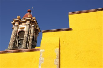 Mexico, Bajio, San Miguel de Allende, Part view of bright yellow exterior wall and church bell