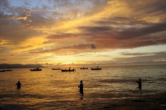Mexico, Jalisco, Puerto Vallarta, Fishermen standing in sea with fishing boats at sunset. Photo :