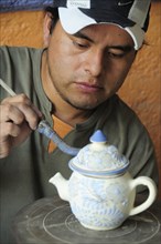 Mexico, Puebla, Talavera ceramic artist at Armando Gallery applying blue detail to raised design on