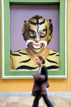 Mexico, Puebla, Young girl walking past poster of wrestler wearing mask and costume. Photo : Nick