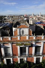Mexico, Puebla, View across city rooftops with red brick and white facade of building in foreground